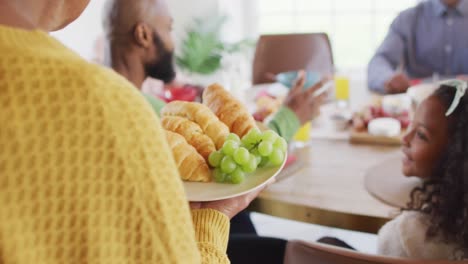 video of happy african american parents, daughter and grandparents serving food and sitting at table