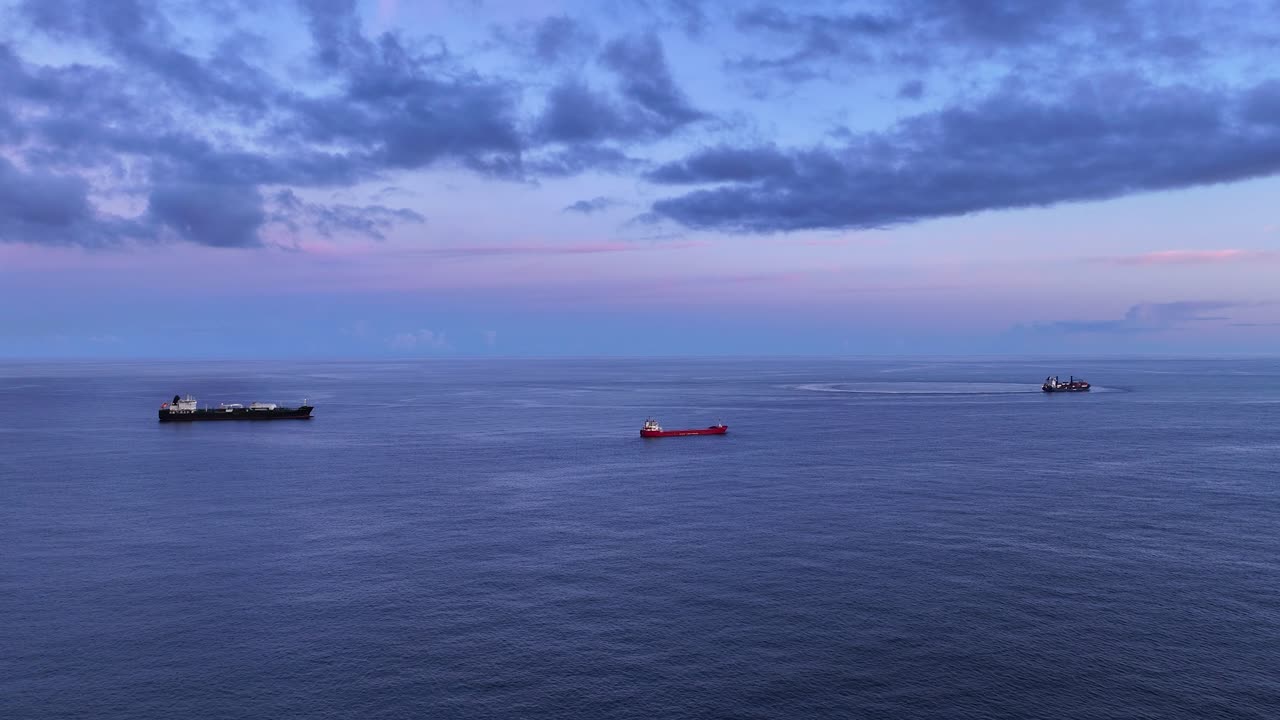 Commercial container ships anchored in open ocean at blue hour, drone dolly in