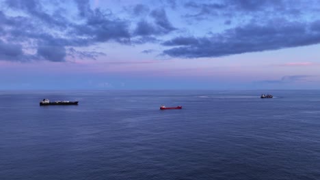 commercial container ships anchored in open ocean at blue hour, drone dolly in