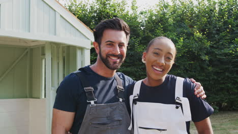 Portrait-Of-Male-Carpenter-With-Female-Apprentice-Building-Outdoor-Summerhouse-In-Garden