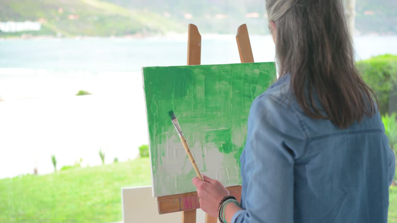 大きな窓の隣のキャンバスに緑の筆致で描かれた絵筆。風景画が作品にインスピレーションを与えている
