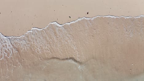 Aerial-view-waves-break-on-white-sand-beach-at-sunset