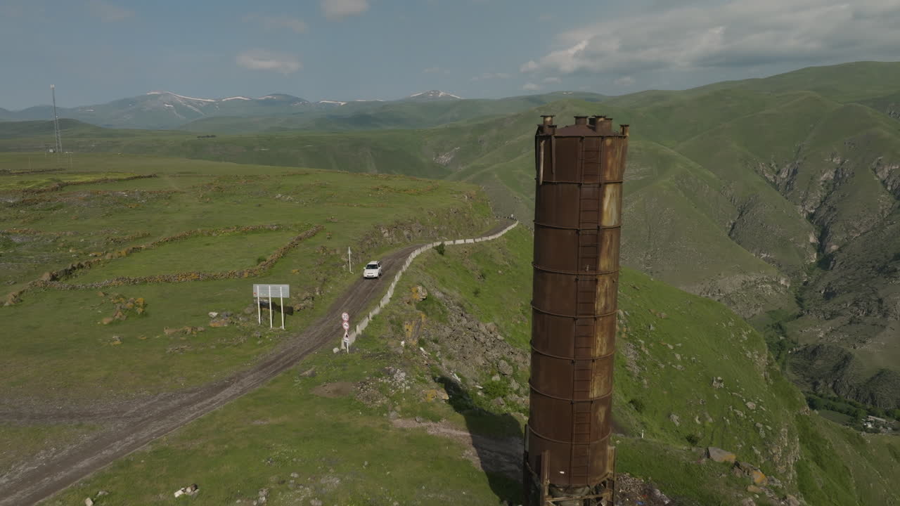 conducción de automóviles en la carretera en el valle de mtkavari con una antigua torre de agua oxidada cerca de apnia, georgia