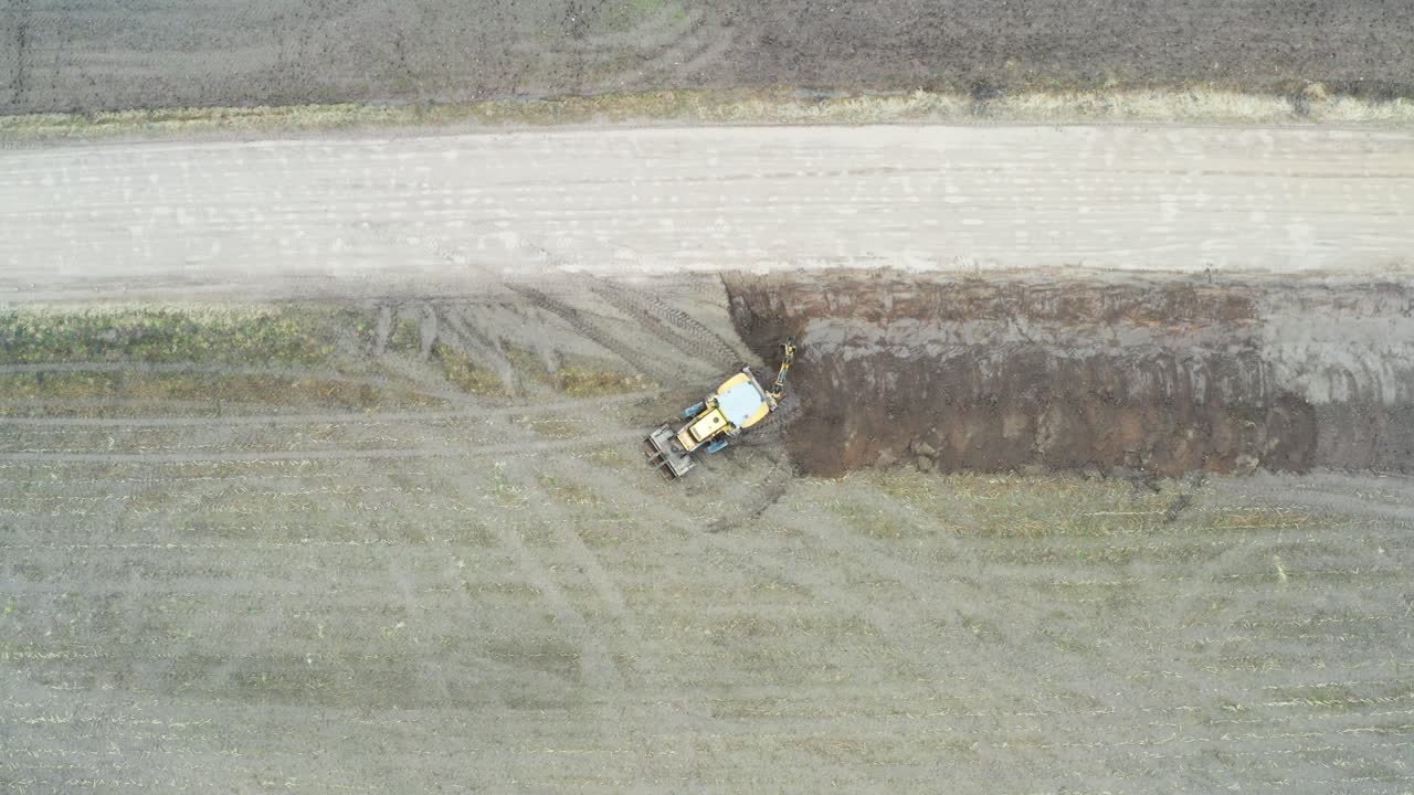 aérea de arriba hacia abajo desciende sobre tractor excavadora cavar zanja de drenaje cerca de la carretera