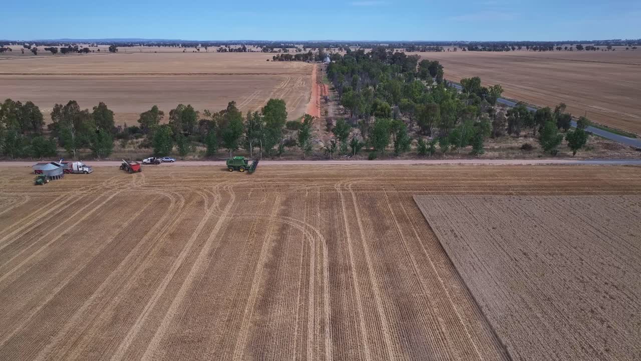 Overhead pullback over farm equipment and a harvester working in a field near Yarrawonga, Victoria, Australia