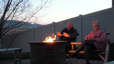 senior, retired couple at a fire pit - wife using a smartphone