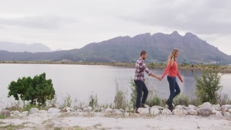 Caucasian-couple-having-a-good-time-on-a-trip-to-the-mountains,-walking-near-lake-and-holding-hands