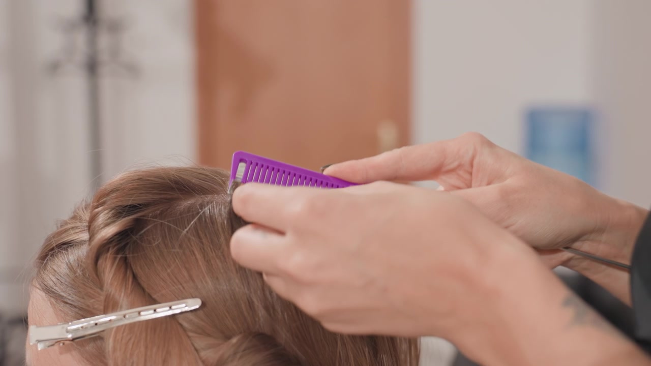 Black colorist applying foil highlights with clips and brush, closeup of brown hair sectioning and product application, focused technique in modern salon interior, careful processing and precise
