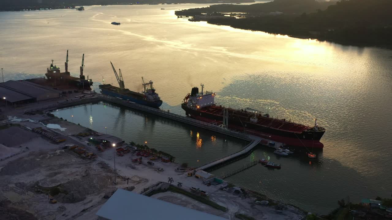 la vista de los pájaros vuela alrededor del parque industrial del puerto de lumut a lo largo del río sungai manjung con barcos comerciales de graneles atracados en el puerto, la inclinación hacia arriba revela el paisaje montañoso al atardecer, perak, malasia