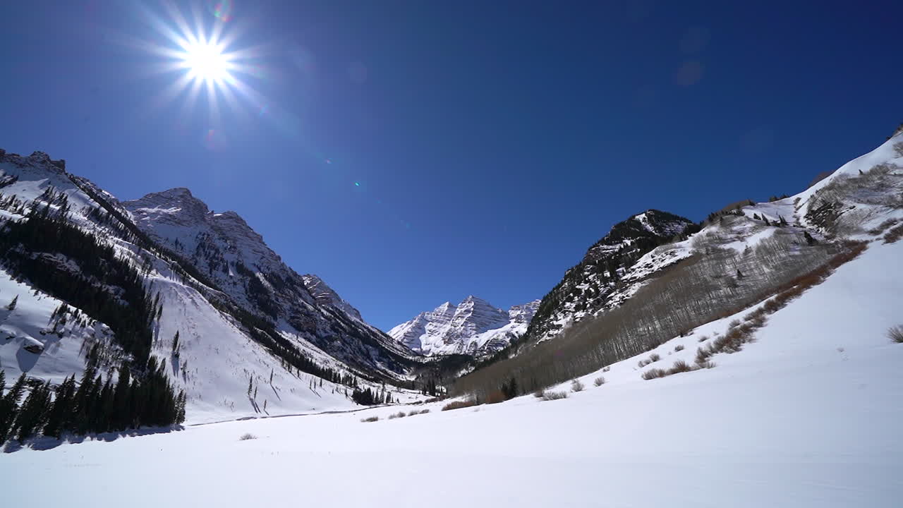 Mid Winter valley landscape view Maroon Bells Aspen Wilderness Colorado bluebird early morning fresh snow with sun flare pan left