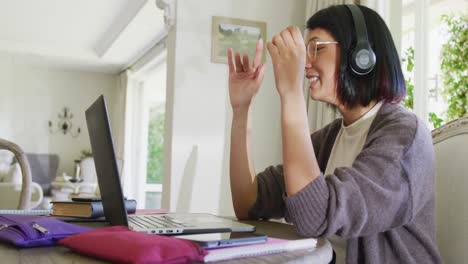 Happy-biracial-teenager-girl-sitting-at-table-and-using-laptop,-in-slow-motion