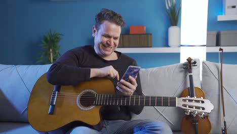 happy male artist, musician looking at phone at home happy and cheerful.