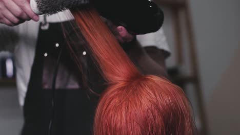 peluquero secando el cabello rojo de una clienta en una peluquería