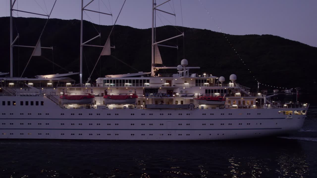 Luftfoto af det sejlende krydstogtskib MSY Wind Surf ved solopgang i Kotorbugten i Kotor, Montenegro med betagende solopgangsbelysning, rolig atmosfære, droneoptagelser i høj kvalitet der viser smukke landskaber.
