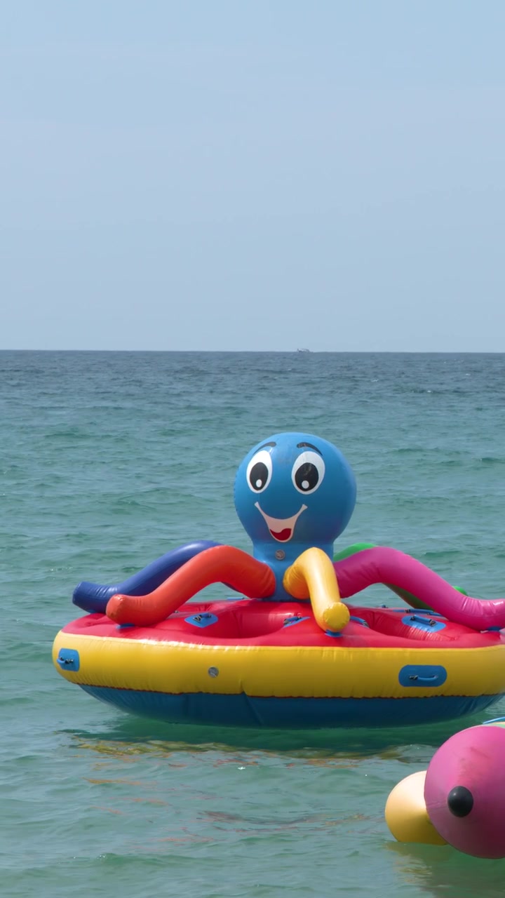 A colorful octopus-shaped inflatable float bobbing on calm turquoise ocean water under bright sunlight