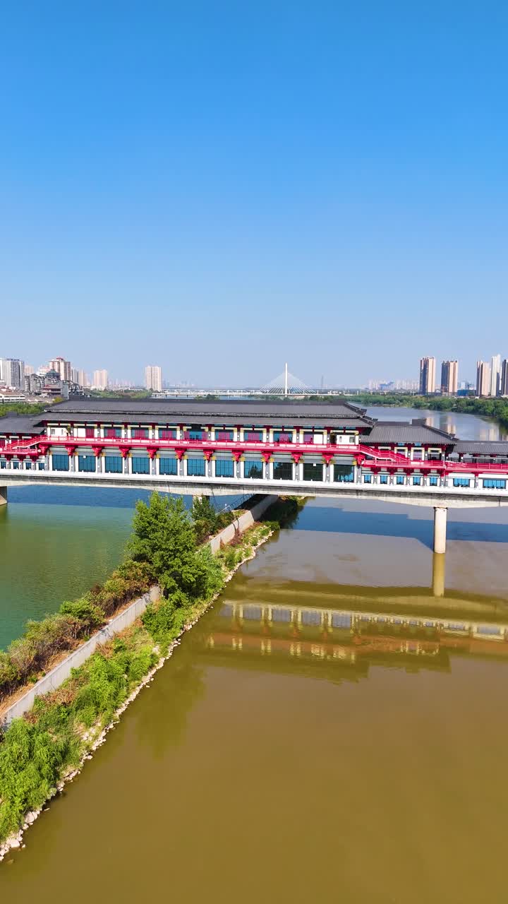 Vertical aerial view crossing the Weihe River in Xi'an, Shaanxi Province, China, showcasing a traditional bridge under bright daytime sunshine, surrounded by scenic landscapes and calm waters.