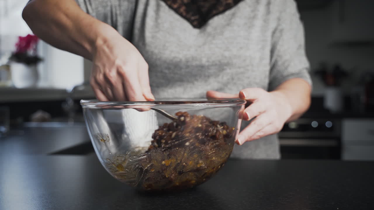 Una donna mescola il ripieno di mince pie in una ciotola di vetro trasparente mentre inforna nella sua cucina.
