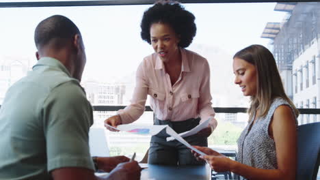 Multi-Cultural-Business-Team-Meeting-Around-Office-Boardroom-Table-With-Laptops-Discussing-Documents