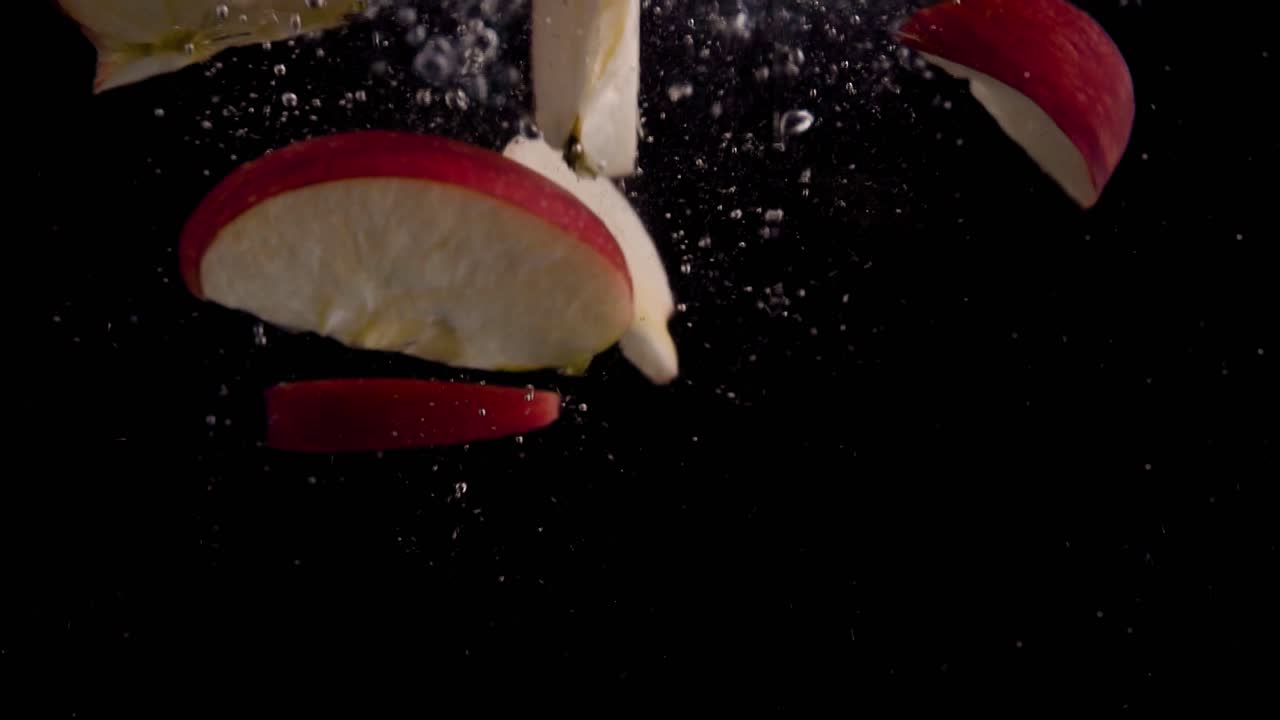 rebanadas de manzana cayendo en cámara superlenta de agua, fondo negro, muchas burbujas de aire, 4k240fps