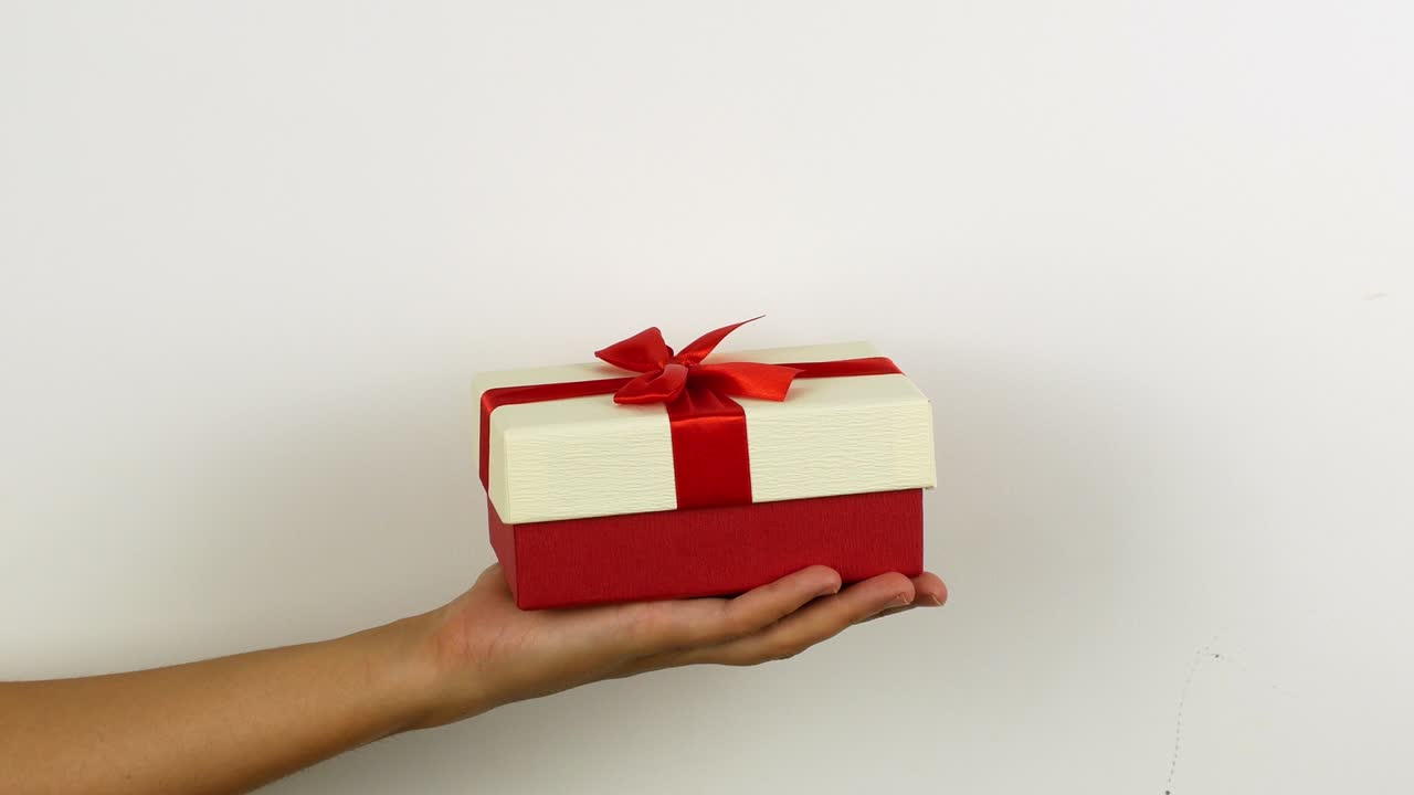 mujer con la mano sosteniendo un regalo para feliz navidad. regalo de año nuevo y navidad en cajas brillantes con un arco sorpresa. video en 4k de un primer plano de una caja de regalos.