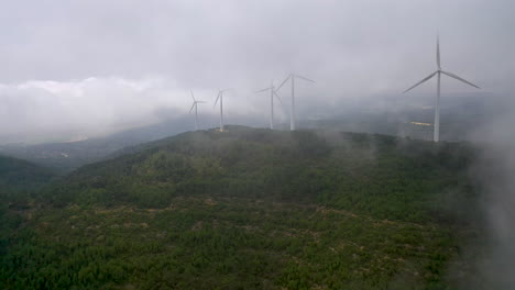 rotating wind turbines on mountain ridge - drone view through misty weather