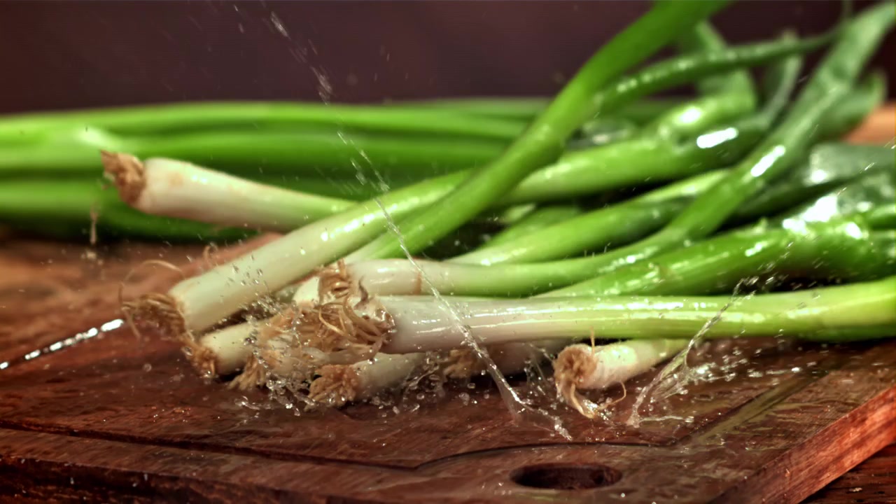 Verse lente-uitjes vallen op een natte houten snijplank met waterspatten