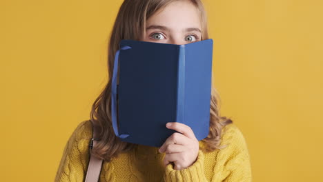 happy teenage caucasian girl student holding notebook in front of her head.