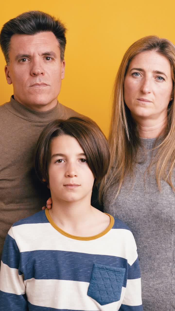Retrato familiar serio de padres e hijo sobre fondo amarillo