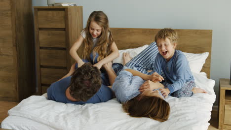 feliz familia amistosa divirtiéndose mientras están acostados y jugando y haciendo cosquillas en la cama en la mañana del fin de semana