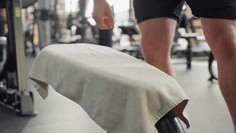 close up of weight bench as gym goer places towel on seat pad before workout showing clean routine and equipment prep in well lit modern fitness space ensuring hygienic environment