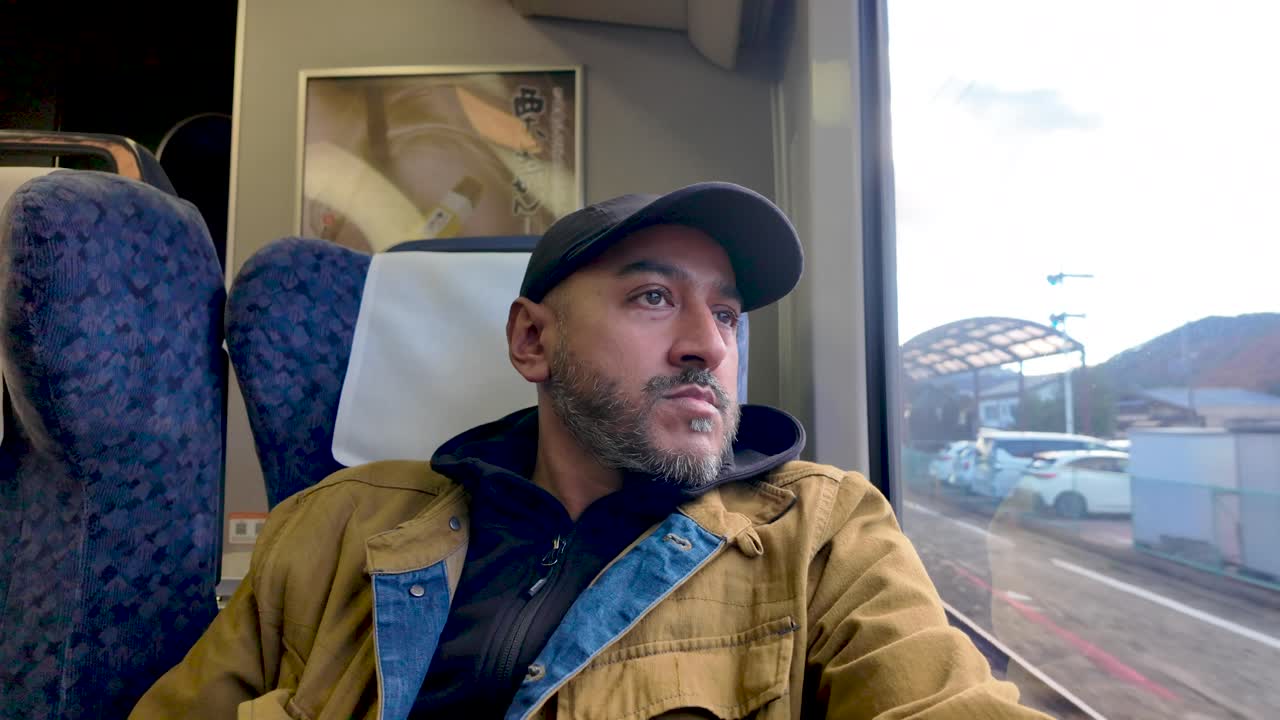 A man sitting inside a train gazing outside, reflecting during a journey.