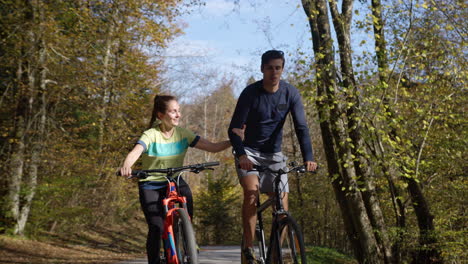 smiling couple having fun cycling uphill through the autumn forest, front view