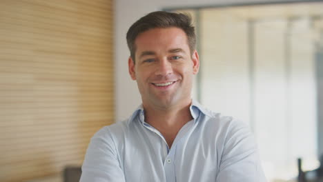 portrait of smiling businessman walking into focus in modern open plan office