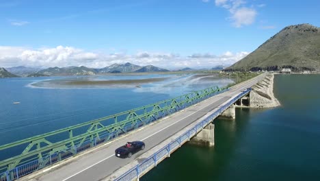 car driving on a bridge over a beautiful lake, surrounded by mountains