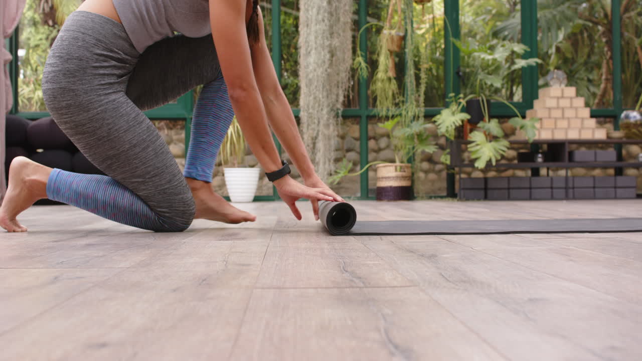 Rolling out yoga mat, woman preparing for yoga session in glass house, copy space