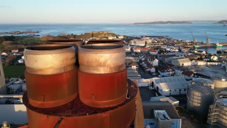 close drone footage of rusty power station chimney with industrial area and vale castle guernsey lit by late afternoon sun and views over the sea to the islands of herm ,jethou and sark