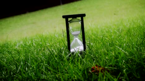 time is running out hourglass sitting in grass during a cloudy and rainy day