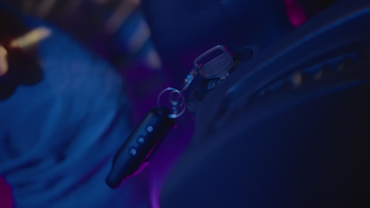 Portachiavi illuminato al neon appeso al sedile, primo piano del portachiavi che oscilla accanto al sedile in pelle mentre una mano si protende per afferrarlo, luci viola e blu creano una tensione cinematografica e dettagli notturni focalizzati all'interno dell'auto