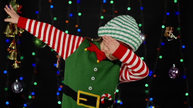 A little girl dressed as an elf dabs in front of a Christmas lights background