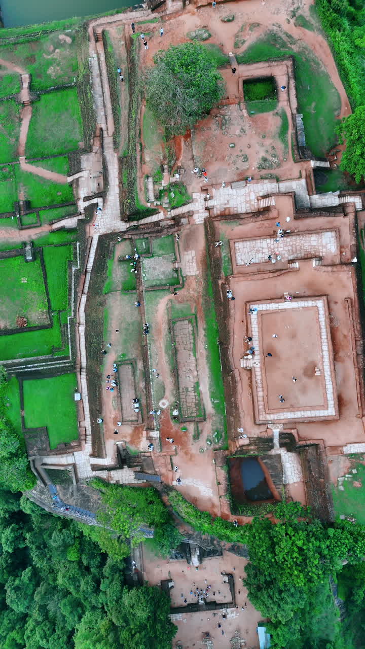 Rising high above the fortress ruins on the mountain top. Lots of tourists walk by the ancient landmark. Sigiriya, Sri Lanka. Vertical video.