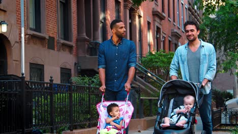 two father friends walking in the street pushing strollers