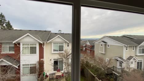 looking out the window of a bedroom of a three story townhouse onto the neighbouring homes and neighbourhood with mountains and grey sky in the background