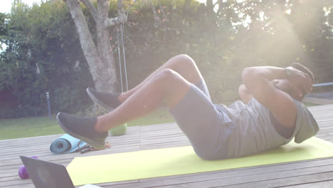 Hombre-Afroamericano-Enfocado-En-Entrenamiento-Físico-Haciendo-Abdominales-En-Cubierta-En-Un-Jardín-Soleado,-Cámara-Lenta