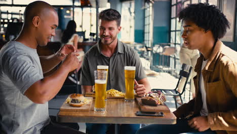 group of male friends meeting up in bar taking photo of food on mobile phone