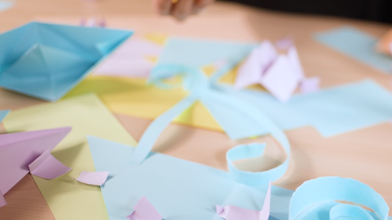 Primo piano di mani che piegano con attenzione carta gialla in origami su un'area di lavoro colorata.