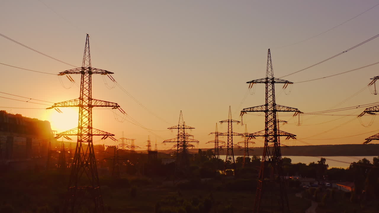 High voltage electrical lines at sunset. Dark silhouette of towers in the rays of the beautiful evening sun. Distribution and supply of electricity. Camera moves back.