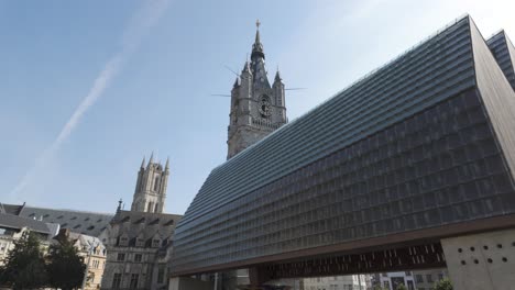 stadshal pavilion contrasting with the historic belfry of ghent on a sunny day. panning shot