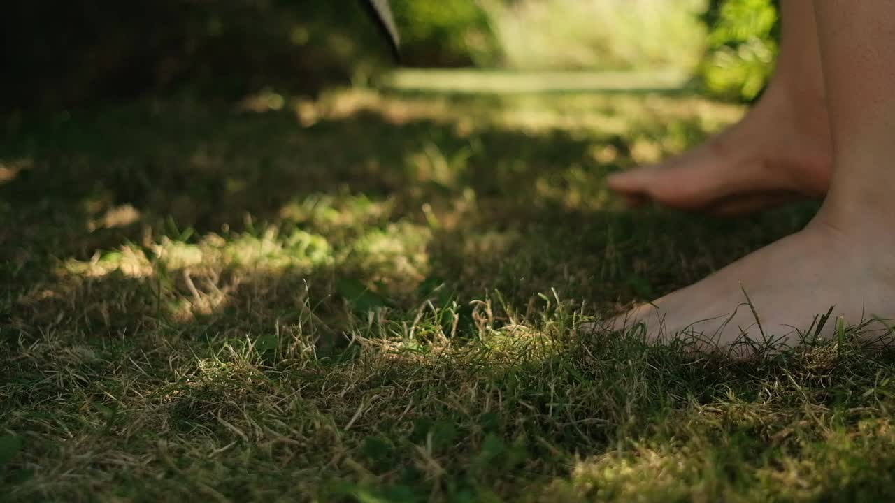 맨발의 여성이 풀밭에서 밀짚모자를 집어 들고 걸어간다