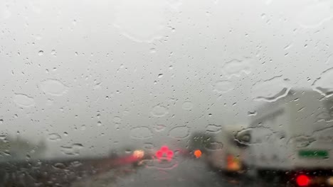 Mal-Tiempo-Lloviendo-Sobre-El-Parabrisas-Con-Semáforos-Rojos-Borrosos-De-Coches-En-El-Fondo-Y-Limpiaparabrisas-Limpiando-El-Parabrisas-De-Las-Gotas-De-Lluvia