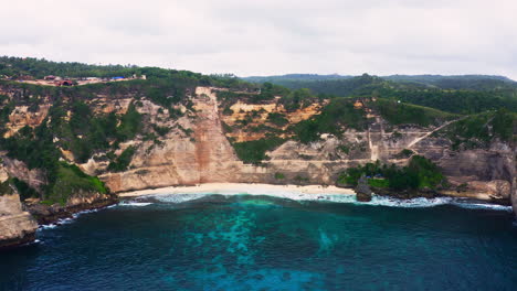 Tropical-Diamond-beach-under-steep-sea-cliff-wall-below-cloudy-sky